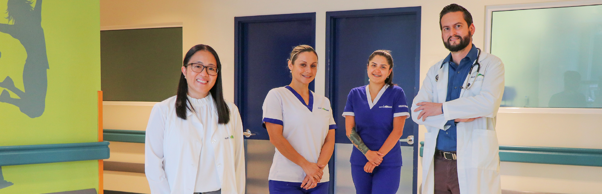 Plano completo de 2 médicos y 2 enfermeras viendo a cámara y sonriendo.